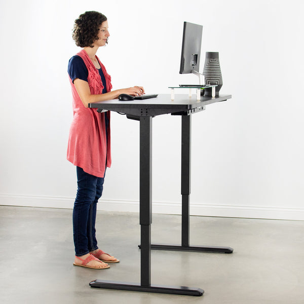 A woman standing and using the standing desk. She is typing on a keyboard on the desk, which has a monitor as well as a mouse.